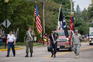 Veterans in diverse uniforms march along a street holding flags